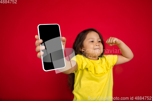 Image of Beautiful emotional little girl isolated on red background. Half-lenght portrait of happy child gesturing