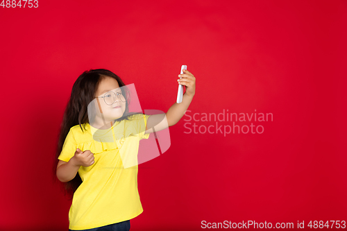 Image of Beautiful emotional little girl isolated on red background. Half-lenght portrait of happy child gesturing