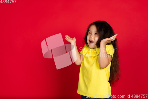 Image of Beautiful emotional little girl isolated on red background. Half-lenght portrait of happy child gesturing