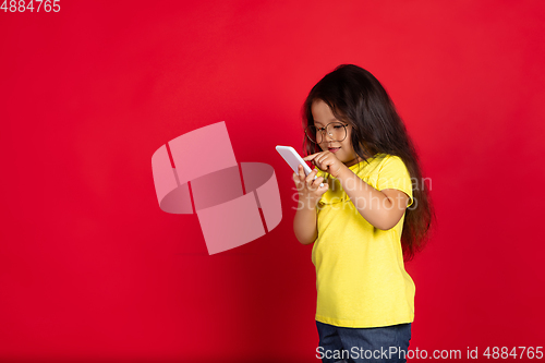 Image of Beautiful emotional little girl isolated on red background. Half-lenght portrait of happy child gesturing