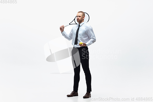 Image of Time for movement. Man in office clothes plays tennis isolated on white studio background.