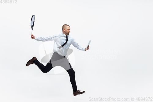 Image of Time for movement. Man in office clothes plays tennis isolated on white studio background.