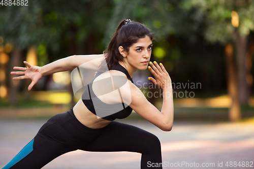 Image of Young female athlete training in the city street in summer sunshine. Beautiful woman practicing, working out. Concept of sport, healthy lifestyle, movement, activity.