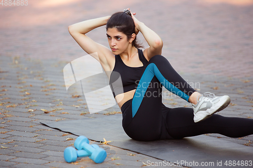 Image of Young female athlete training in the city street in summer sunshine. Beautiful woman practicing, working out. Concept of sport, healthy lifestyle, movement, activity.