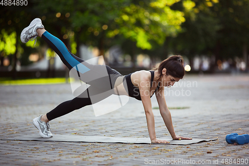 Image of Young female athlete training in the city street in summer sunshine. Beautiful woman practicing, working out. Concept of sport, healthy lifestyle, movement, activity.