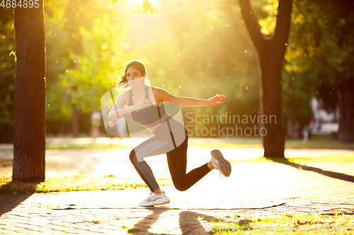 Image of Young female athlete training in the city street in summer sunshine. Beautiful woman practicing, working out. Concept of sport, healthy lifestyle, movement, activity.