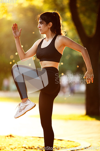 Image of Young female athlete training in the city street in summer sunshine. Beautiful woman practicing, working out. Concept of sport, healthy lifestyle, movement, activity.