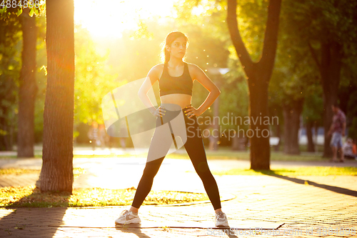 Image of Young female athlete training in the city street in summer sunshine. Beautiful woman practicing, working out. Concept of sport, healthy lifestyle, movement, activity.