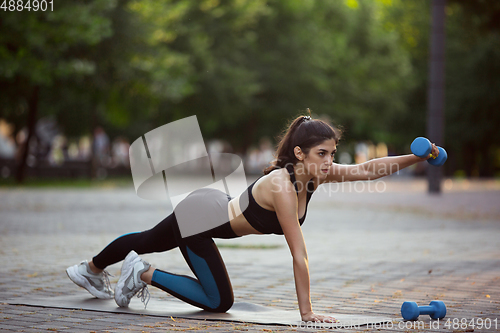 Image of Young female athlete training in the city street in summer sunshine. Beautiful woman practicing, working out. Concept of sport, healthy lifestyle, movement, activity.