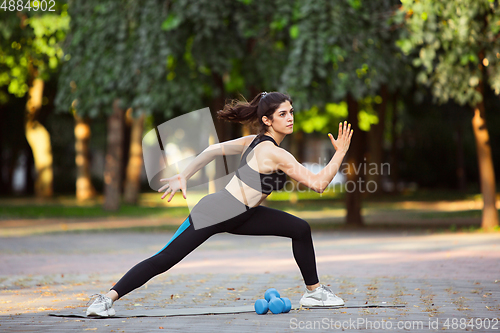 Image of Young female athlete training in the city street in summer sunshine. Beautiful woman practicing, working out. Concept of sport, healthy lifestyle, movement, activity.