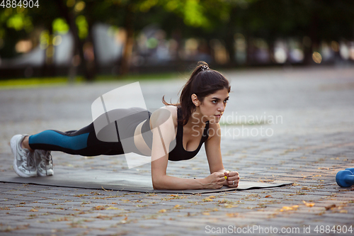 Image of Young female athlete training in the city street in summer sunshine. Beautiful woman practicing, working out. Concept of sport, healthy lifestyle, movement, activity.