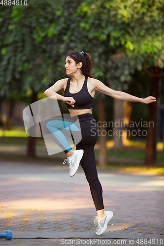 Image of Young female athlete training in the city street in summer sunshine. Beautiful woman practicing, working out. Concept of sport, healthy lifestyle, movement, activity.