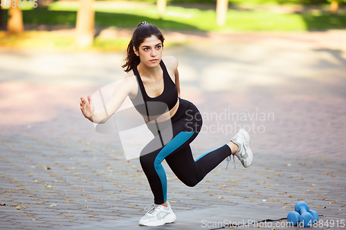 Image of Young female athlete training in the city street in summer sunshine. Beautiful woman practicing, working out. Concept of sport, healthy lifestyle, movement, activity.