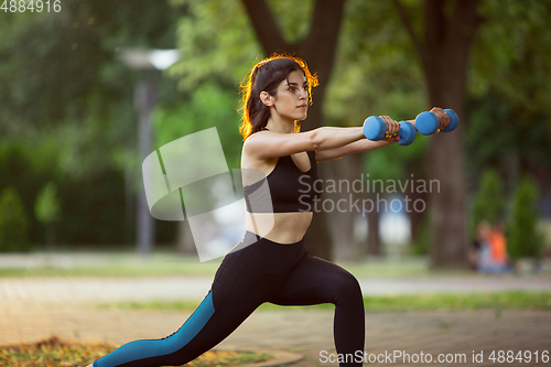 Image of Young female athlete training in the city street in summer sunshine. Beautiful woman practicing, working out. Concept of sport, healthy lifestyle, movement, activity.