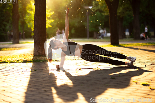 Image of Young female athlete training in the city street in summer sunshine. Beautiful woman practicing, working out. Concept of sport, healthy lifestyle, movement, activity.