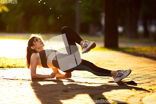 Image of Young female athlete training in the city street in summer sunshine. Beautiful woman practicing, working out. Concept of sport, healthy lifestyle, movement, activity.