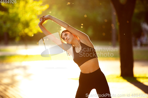Image of Young female athlete training in the city street in summer sunshine. Beautiful woman practicing, working out. Concept of sport, healthy lifestyle, movement, activity.