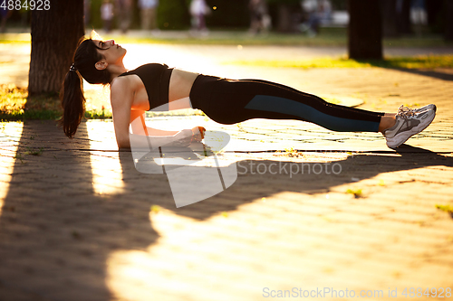 Image of Young female athlete training in the city street in summer sunshine. Beautiful woman practicing, working out. Concept of sport, healthy lifestyle, movement, activity.