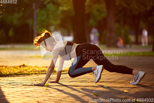 Image of Young female athlete training in the city street in summer sunshine. Beautiful woman practicing, working out. Concept of sport, healthy lifestyle, movement, activity.