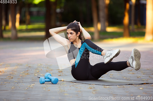 Image of Young female athlete training in the city street in summer sunshine. Beautiful woman practicing, working out. Concept of sport, healthy lifestyle, movement, activity.