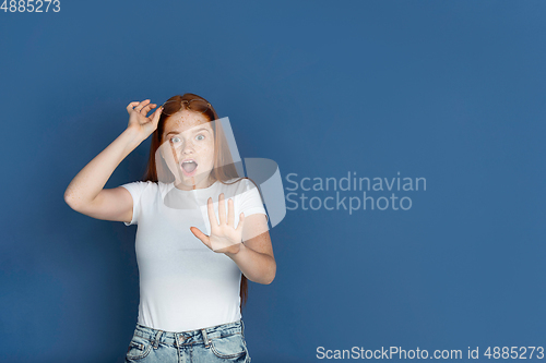 Image of Caucasian young girl\'s portrait isolated on blue studio background. Beautiful female model. Concept of human emotions, facial expression, sales, ad, youth culture.