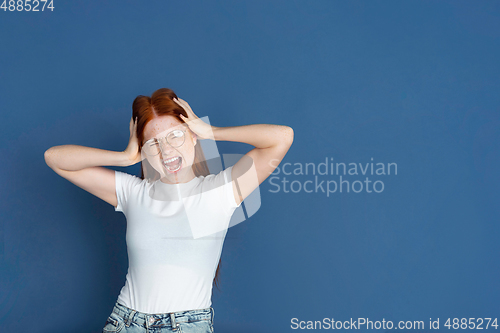 Image of Caucasian young girl\'s portrait isolated on blue studio background. Beautiful female model. Concept of human emotions, facial expression, sales, ad, youth culture.