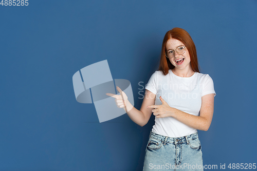 Image of Caucasian young girl\'s portrait isolated on blue studio background. Beautiful female model. Concept of human emotions, facial expression, sales, ad, youth culture.