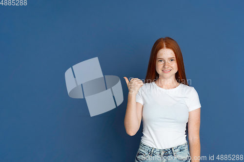 Image of Caucasian young girl\'s portrait isolated on blue studio background. Beautiful female model. Concept of human emotions, facial expression, sales, ad, youth culture.