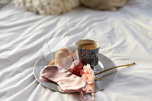 Image of croissant, coffee and eye sleeping mask in bed