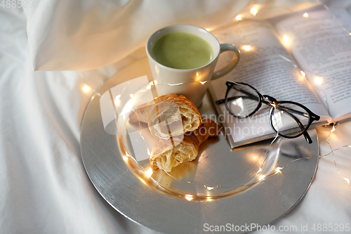 Image of croissants, matcha tea, book and glasses in bed