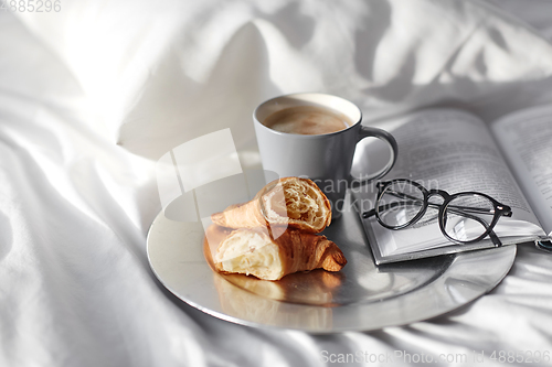 Image of croissants, cup of coffee and book in bed at home