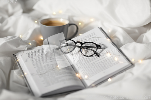 Image of cup of coffee, book, glasses and garland in bed