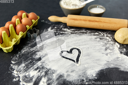 Image of heart on flour, rolling pin, eggs and dough