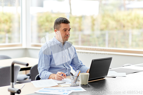 Image of man in earphones with laptop working at home