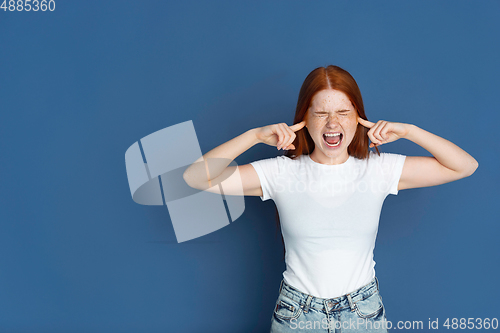 Image of Caucasian young girl\'s portrait isolated on blue studio background. Beautiful female model. Concept of human emotions, facial expression, sales, ad, youth culture.