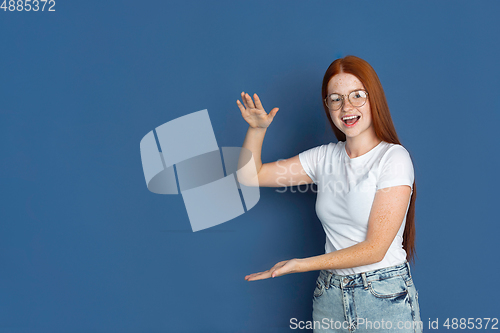 Image of Caucasian young girl\'s portrait isolated on blue studio background. Beautiful female model. Concept of human emotions, facial expression, sales, ad, youth culture.