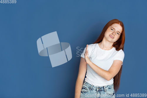 Image of Caucasian young girl\'s portrait isolated on blue studio background. Beautiful female model. Concept of human emotions, facial expression, sales, ad, youth culture.