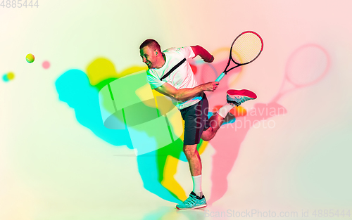 Image of Caucasian male professional sportsman playing tennis on studio background in neon light