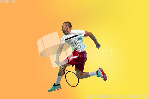 Image of Caucasian male professional sportsman playing tennis on studio background in neon light