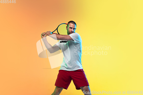 Image of Caucasian male professional sportsman playing tennis on studio background in neon light