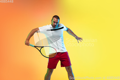 Image of Caucasian male professional sportsman playing tennis on studio background in neon light