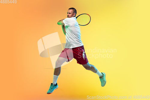 Image of Caucasian male professional sportsman playing tennis on studio background in neon light