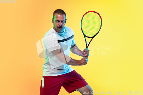 Image of Caucasian male professional sportsman playing tennis on studio background in neon light