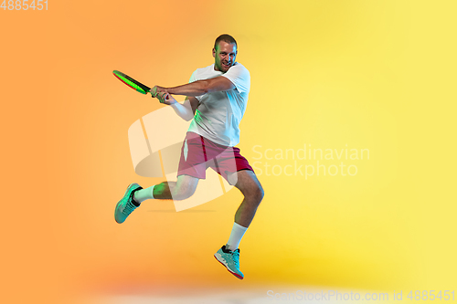 Image of Caucasian male professional sportsman playing tennis on studio background in neon light