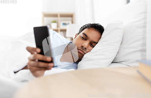 Image of sleepy indian man with smartphone lying in bed