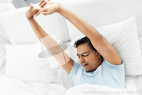 Image of sleepy indian man stretching in bed at home