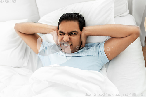 Image of annoyed indian man lying in bed and closing ears