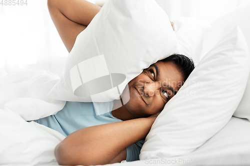Image of annoyed indian man lying in bed and closing ears