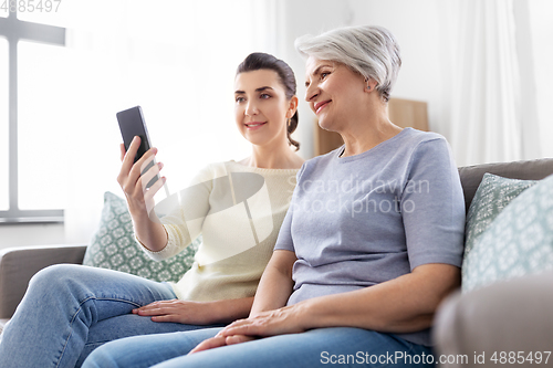 Image of senior mother with daughter taking selfie at home