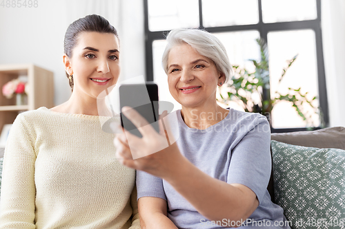 Image of senior mother with daughter taking selfie at home